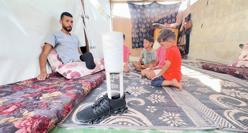إبراهيم عبد النبي، النازح الفلسطيني في غزة، يجلس مع أبنائه وهو ينظر إلى الطرف الاصطناعي الذي صنعه ليعوضه فقدان إحدى قدميه.